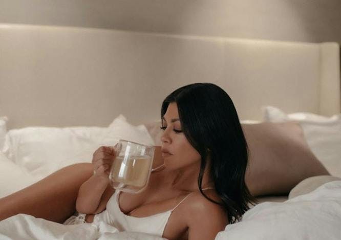 Kourtney Kardashian lying on a bed sipping a drink.