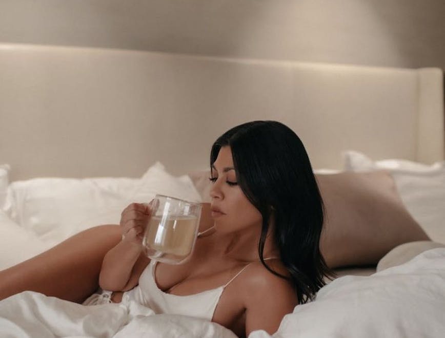 Kourtney Kardashian lying on a bed sipping a drink.