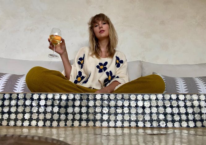 taylor swift wearing a sweater with blue flowers and drinking wine
