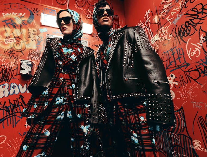 Male and female model in matching red and black plaid suits with blue florals and studded leather jackets.
