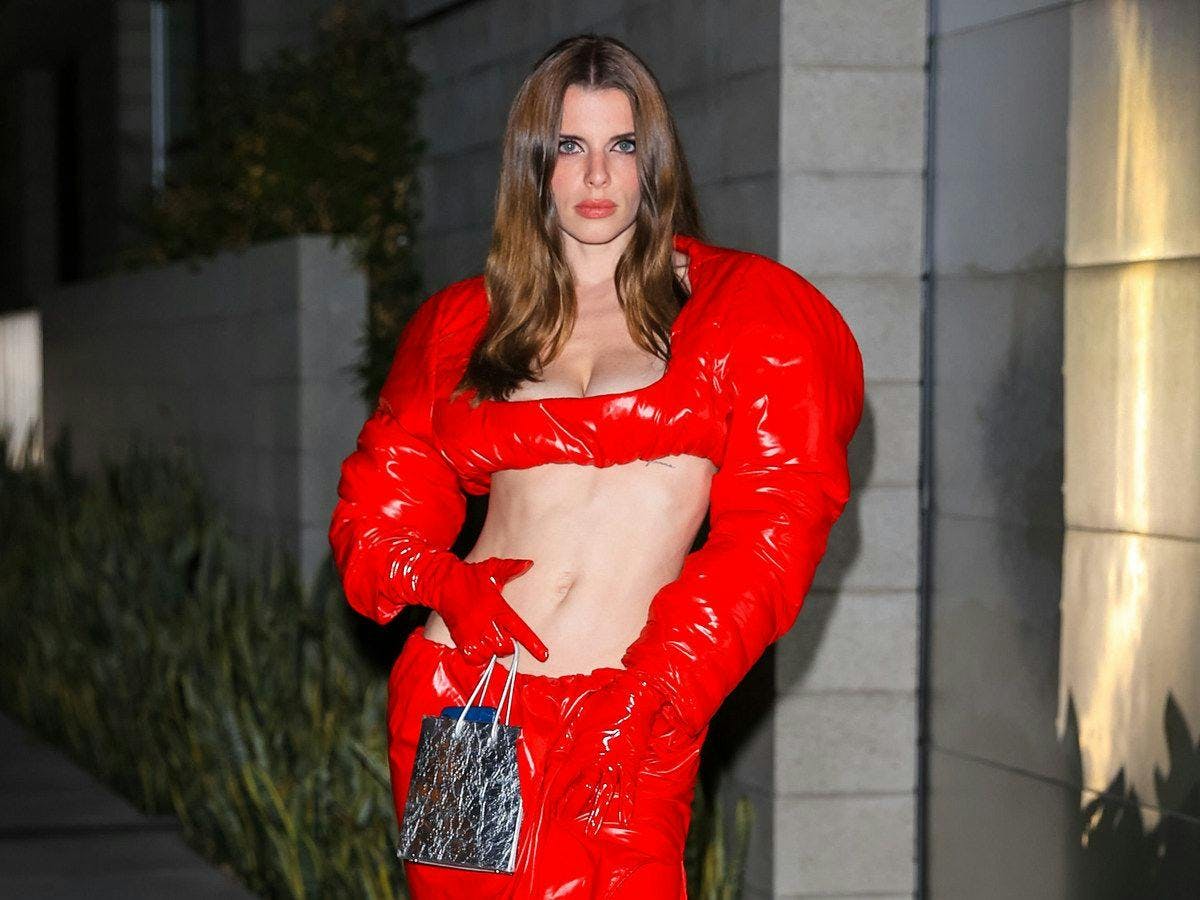Julia Fox wearing a cropped red top with puff sleeves and matching red gloves while holding a mini purse.