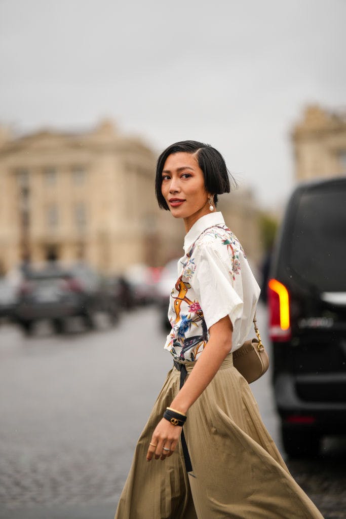Woman walking down the street in a printed blouse and flowy light brown pants.