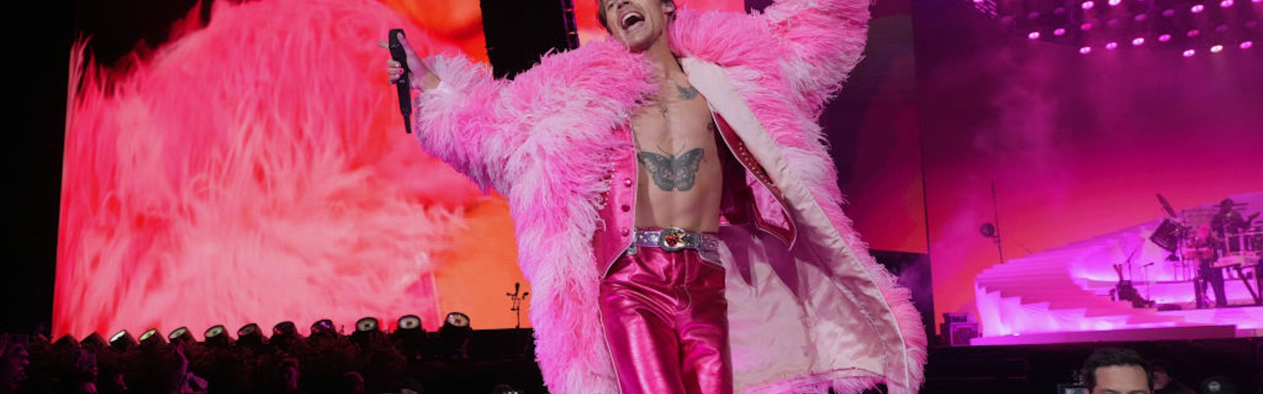 Harry Styles in a pink feather coat, vest, pants.