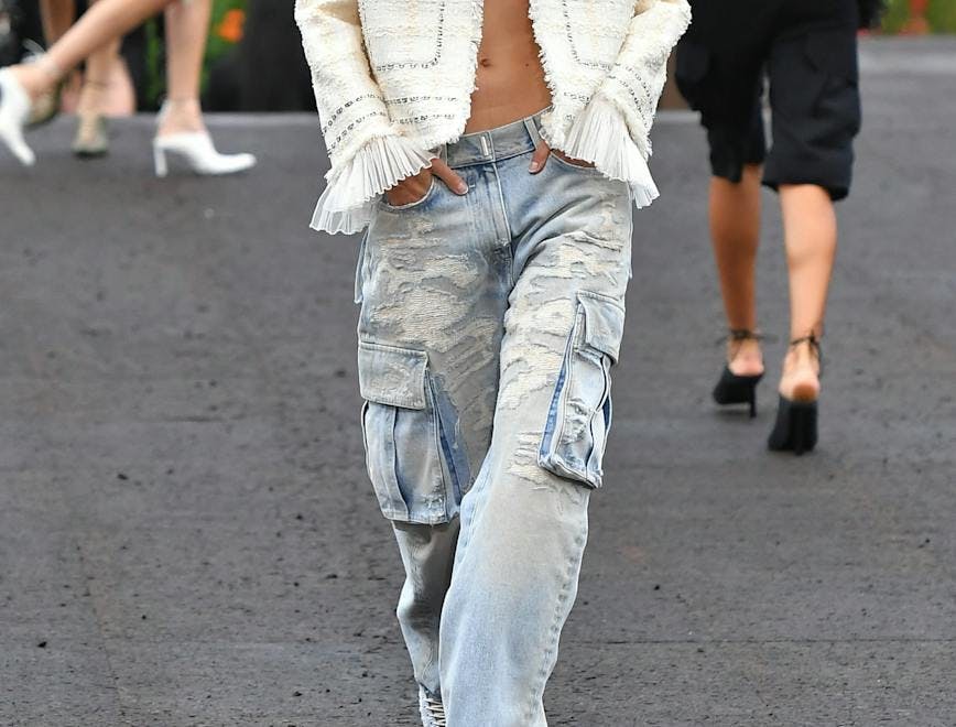 A model in a white jacket and baggy blue jeans.