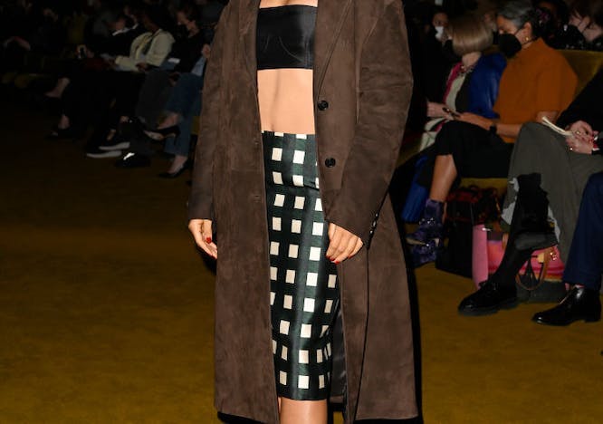 Woman in a black bandeau top, checkered midi skirt, and brown coat.