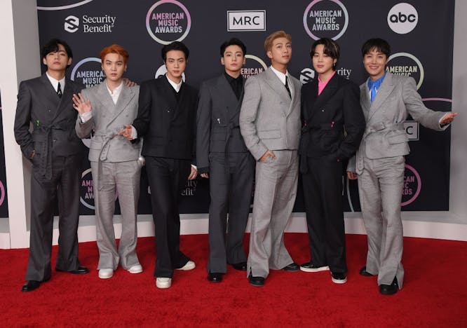 A group of guys in grey and black suits while standing on a red carpet.
