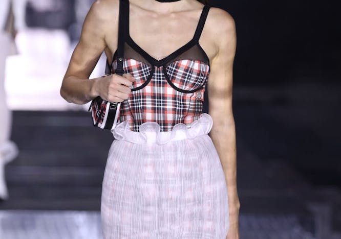 A woman in a plaid top and white skirt.