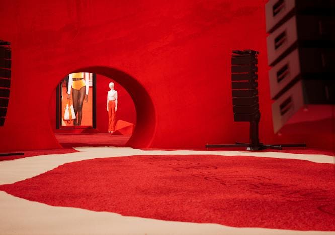 A runway with white marble, red carpet, and manequin in red pants in a red room