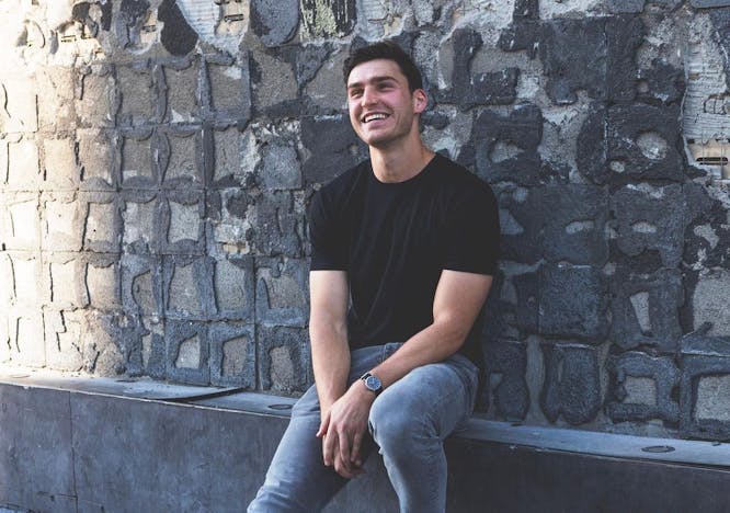 A guy in a black shirt and jeans smiling.