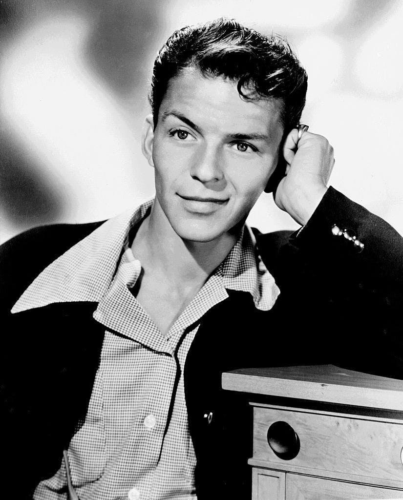 A young guy looking at the camera while wearing a black cardigan and collared shirt.
