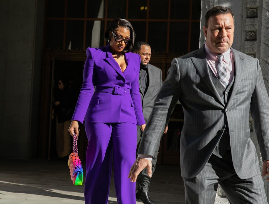 A woman in a bright purple suit walking behind a man in a grey suit.