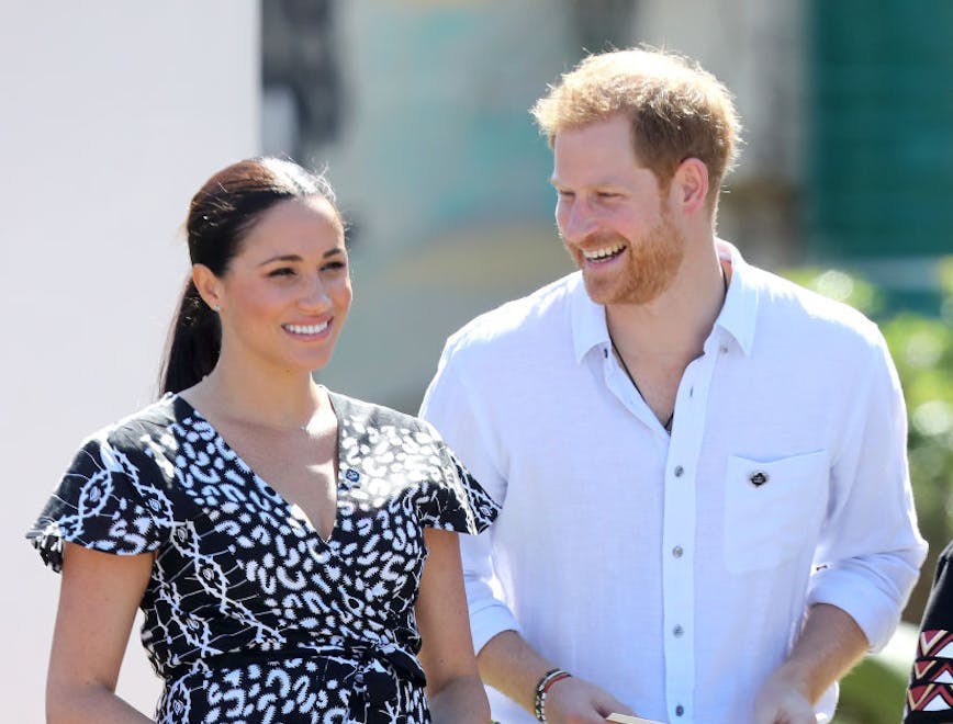 Meghan Markle in a black dress next to Prince Harry in a white dress shirt and dark pants.