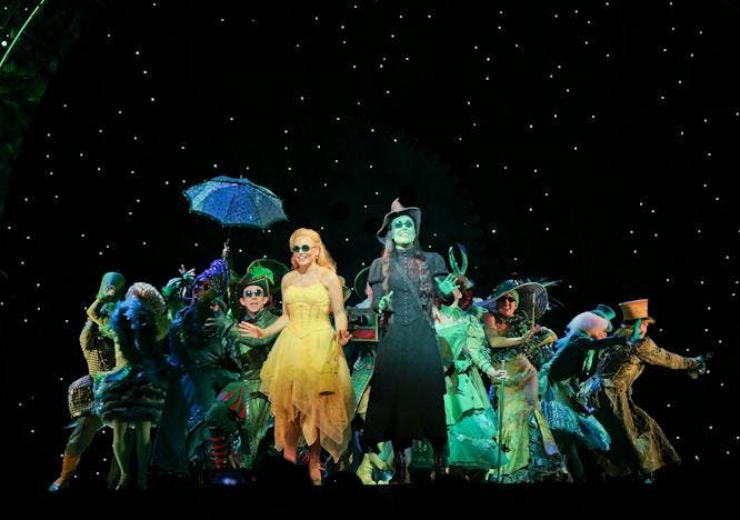 Wicked cast on stage in green Glinda in yellow dress black backdrop