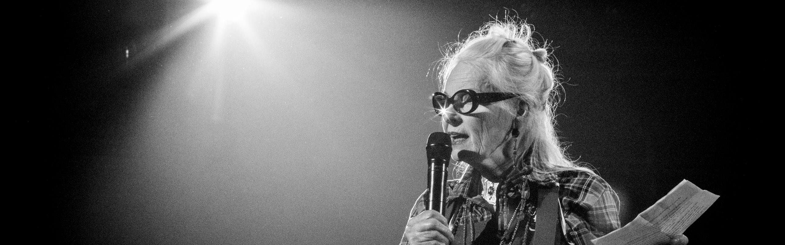 Black and white photo Vivienne Westwood with a microphone under a spotlight
