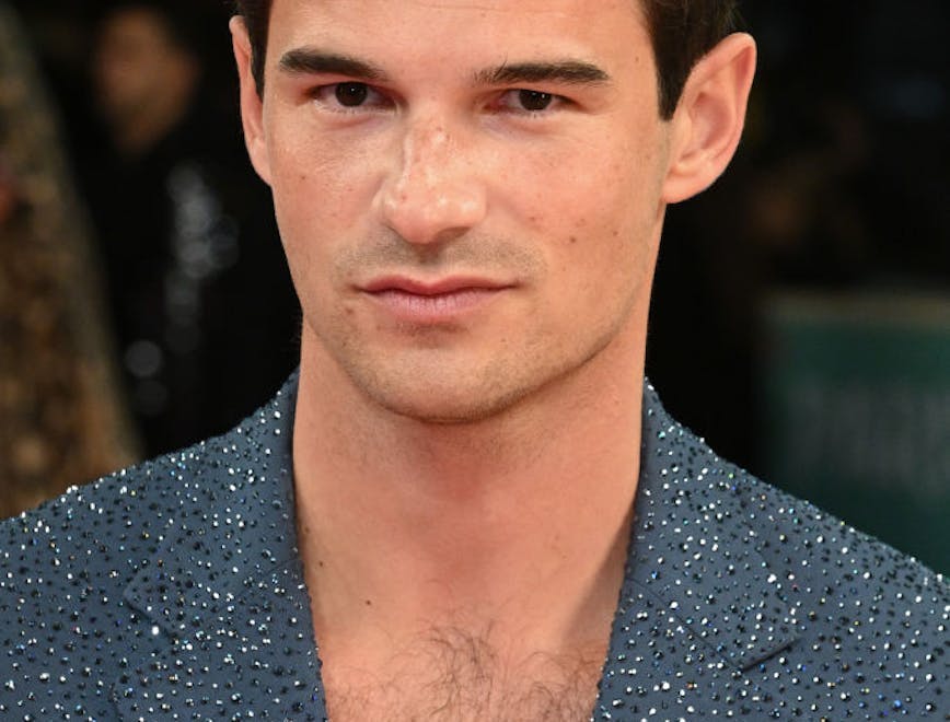 A man looking at the camera while wearing a grey sequined suit and white top.