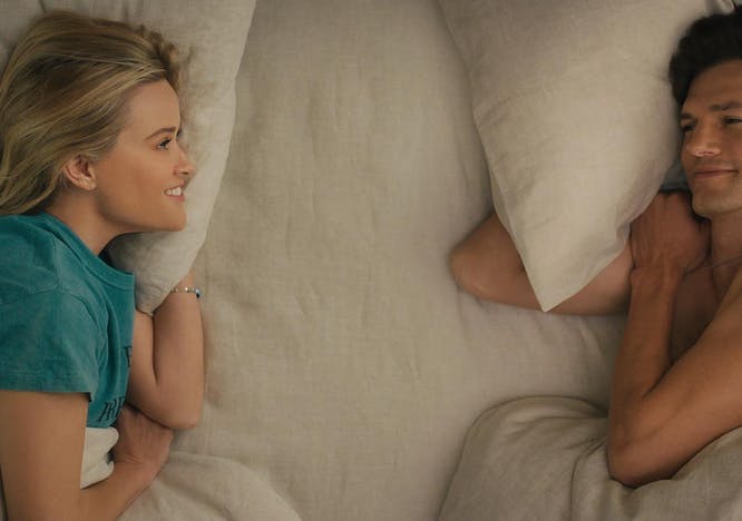 Reese Witherspoon and Ashton Kutcher laying on white, unmade bed.
