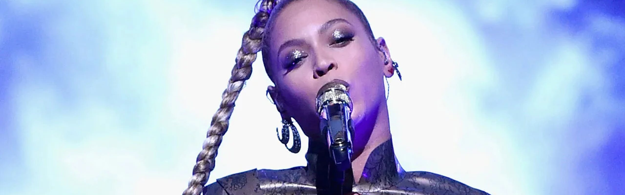 Beyonce on stage with long braid, silver body suit, and knee-high boots.