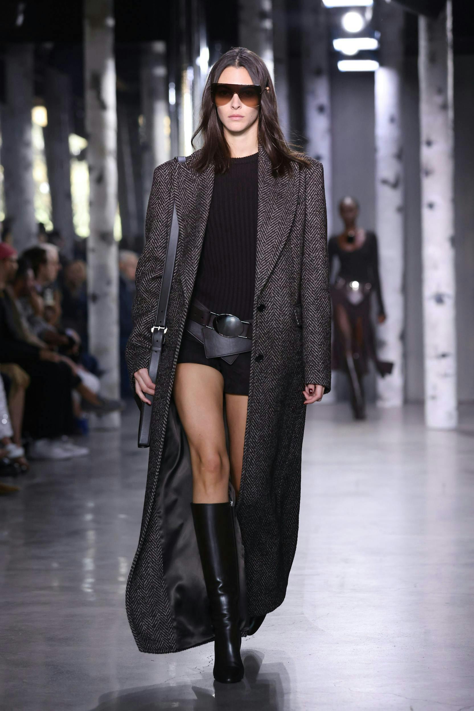 Woman in long trench coat and shorts on runway.
