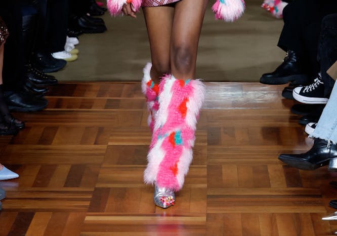 A model in a furry pink jacket, bra top, mini skirt, and boots.