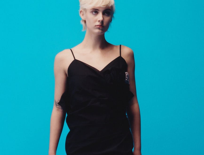 Woman wearing a black slip dress against a blue background.