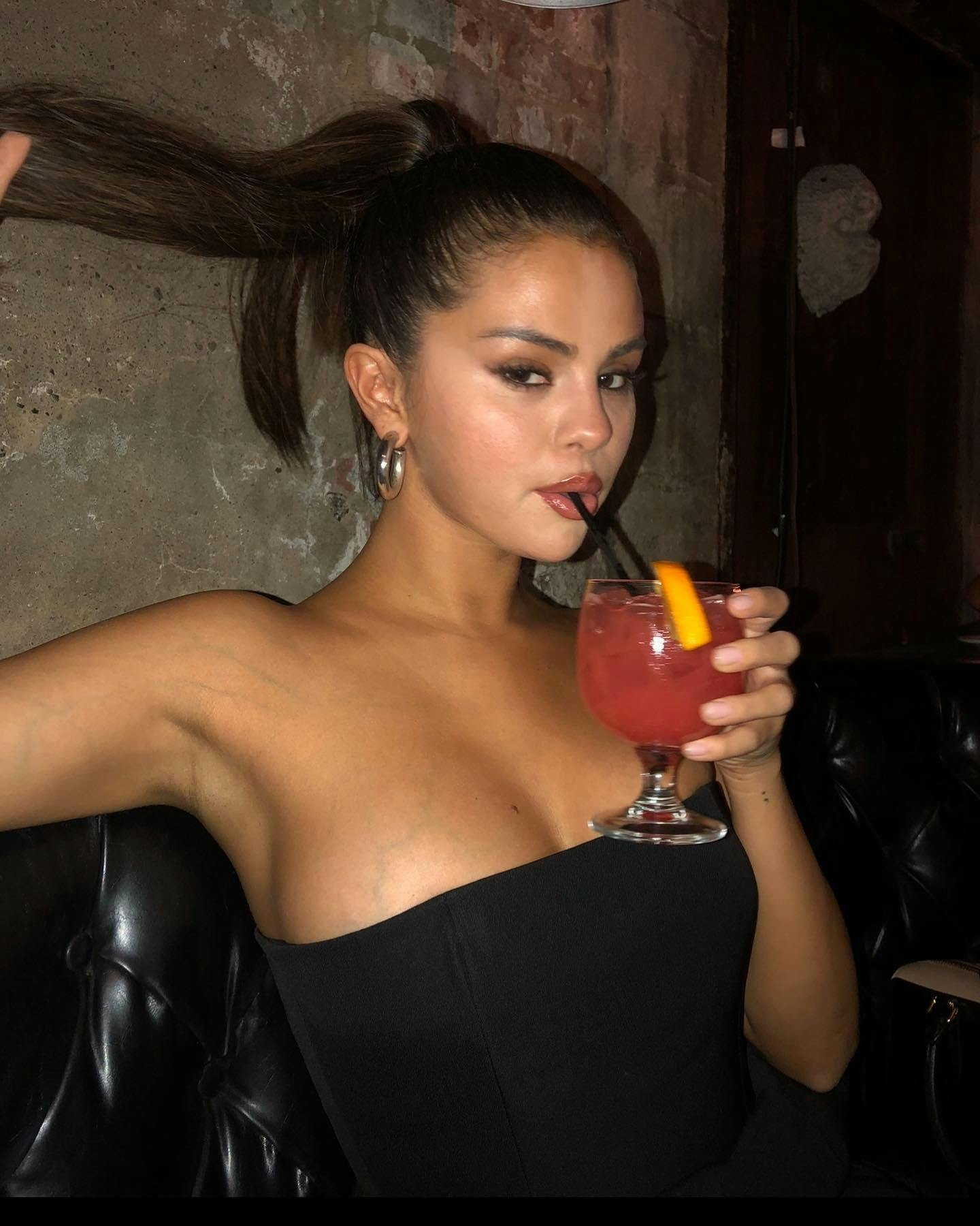 Woman in black dress sipping on a pink drink.