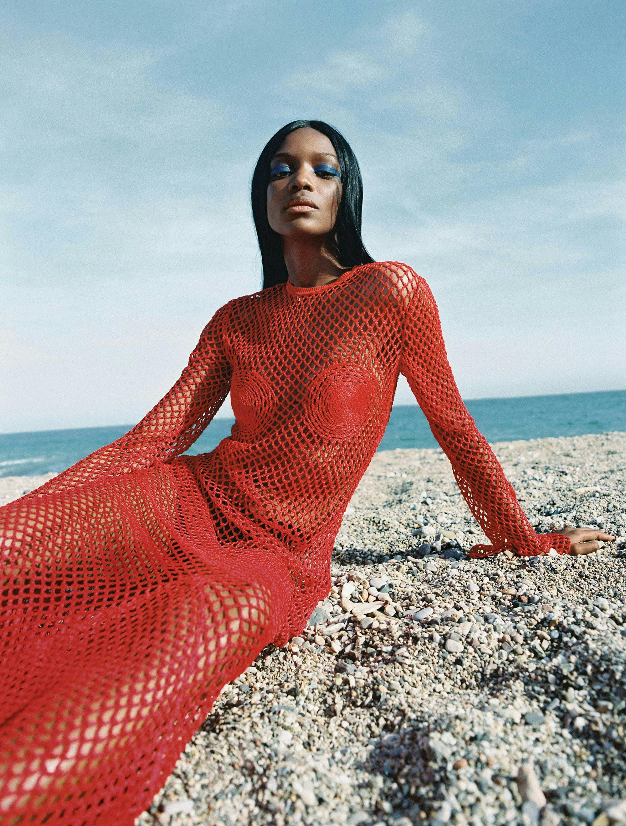 Model in red net dress on the beach.