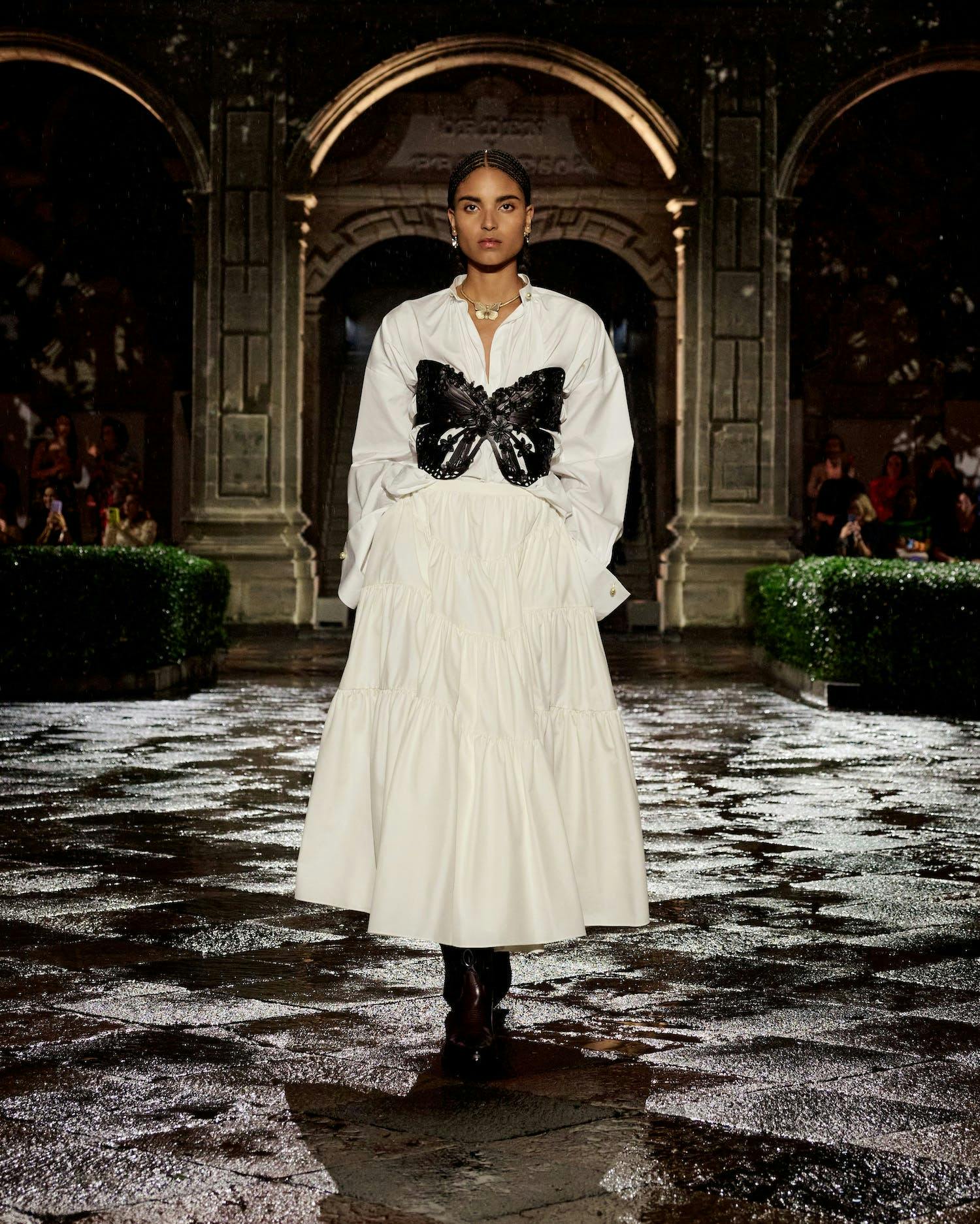 A model walking in a white dress and black butterfly-shaped corset.