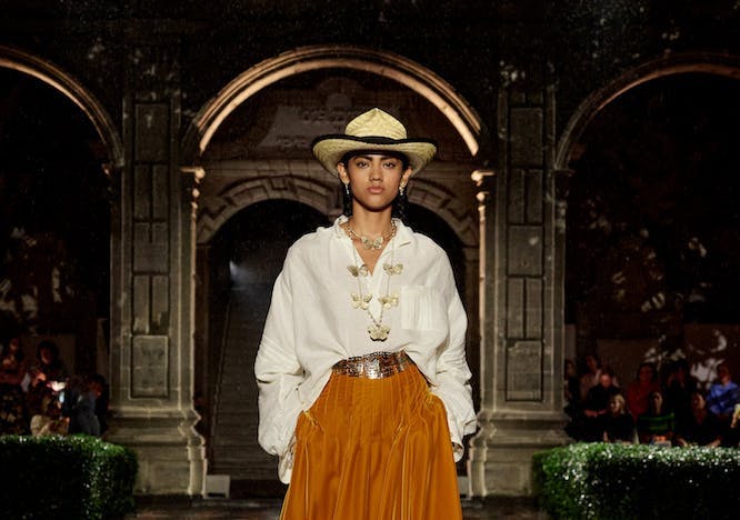 A model walking in a white shirt and orange skirt.