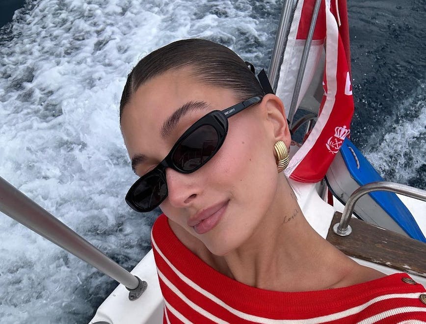 Hailey Bieber in a red striped shirt and sunglasses.