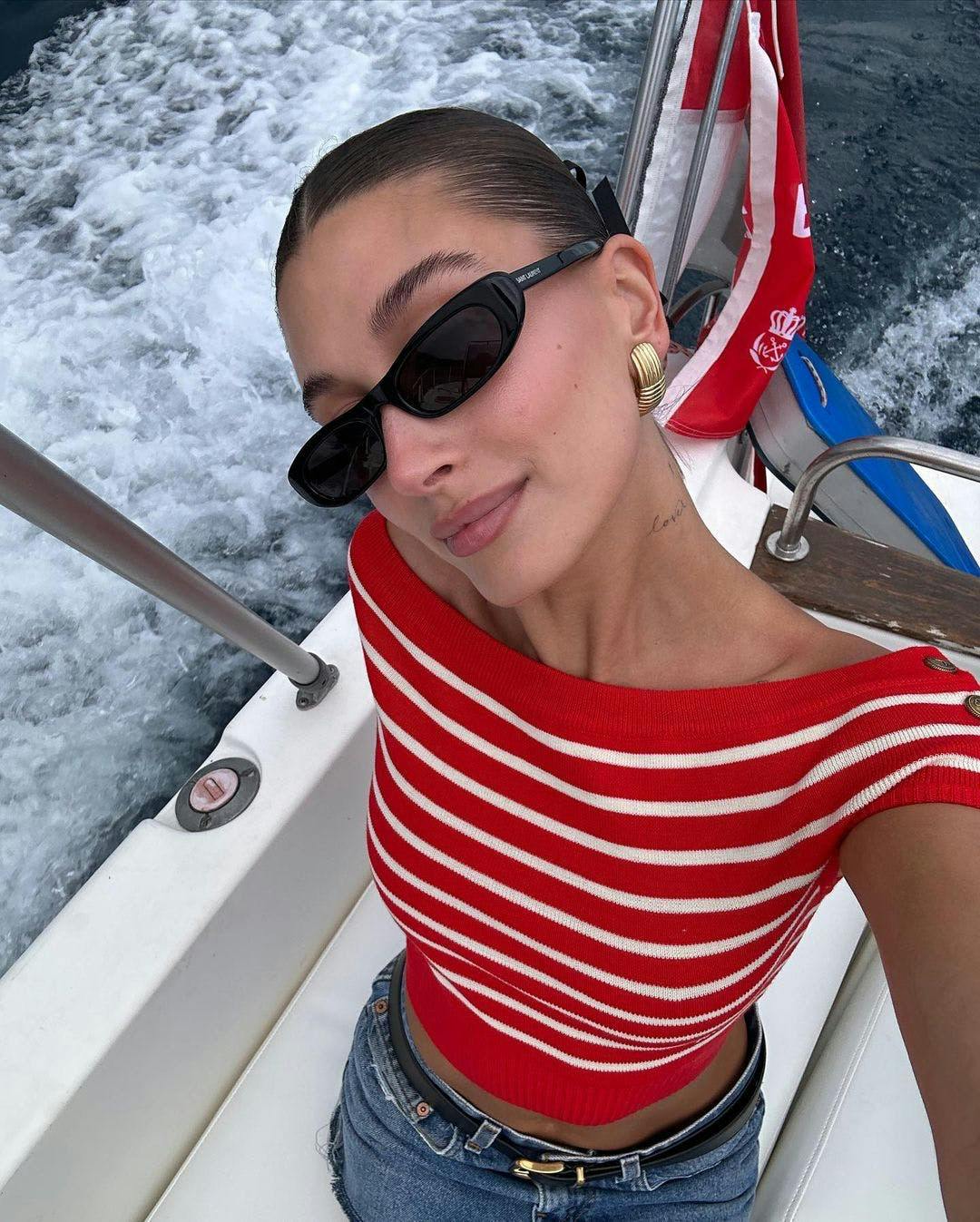 Hailey Bieber in a red striped shirt and sunglasses.