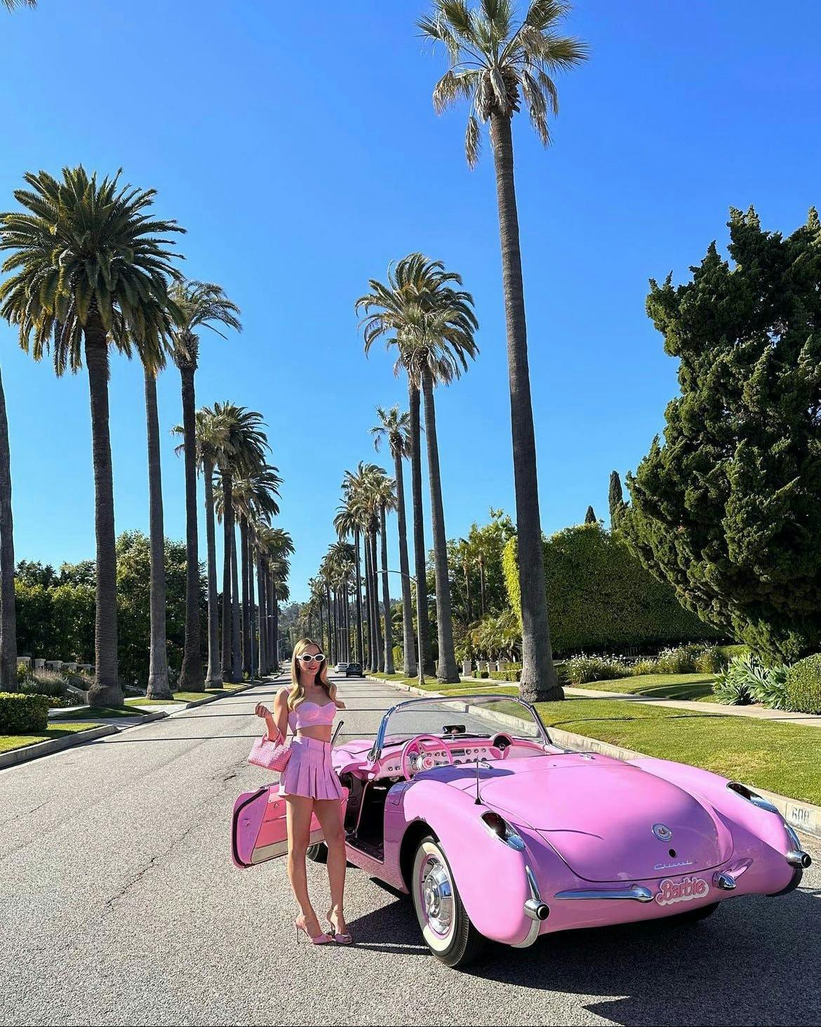 Margot Robbie in a pink set posing with a pink car for Barbie press