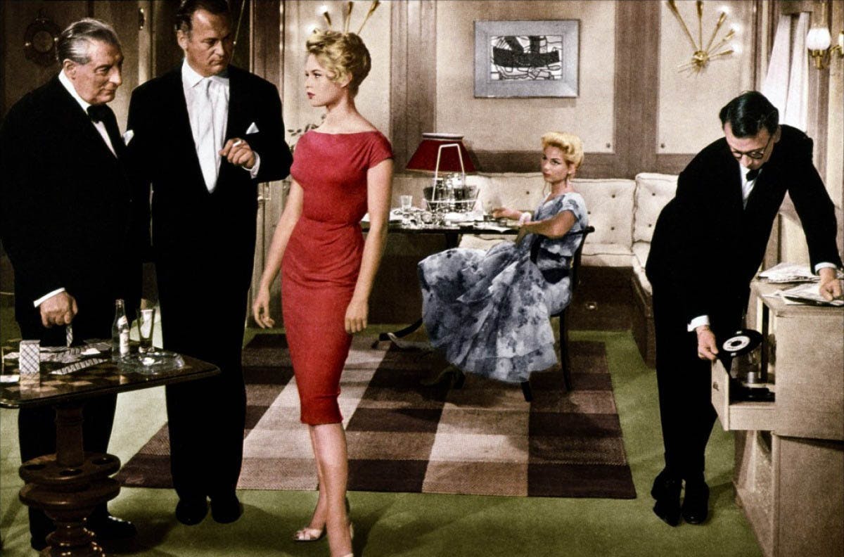 A woman in a red dress and a woman in a blue dress next to men in black suits french girl style icons