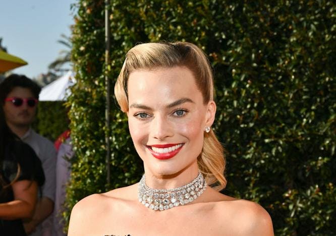 Margot Robbie with a blonde barbie hair and a black strapless gown.