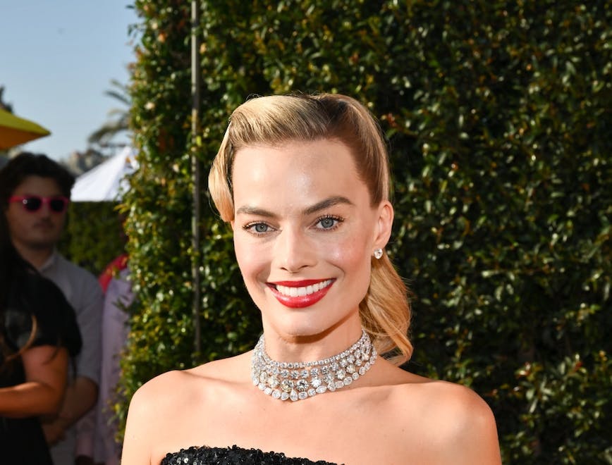 Margot Robbie with a blonde barbie hair and a black strapless gown.