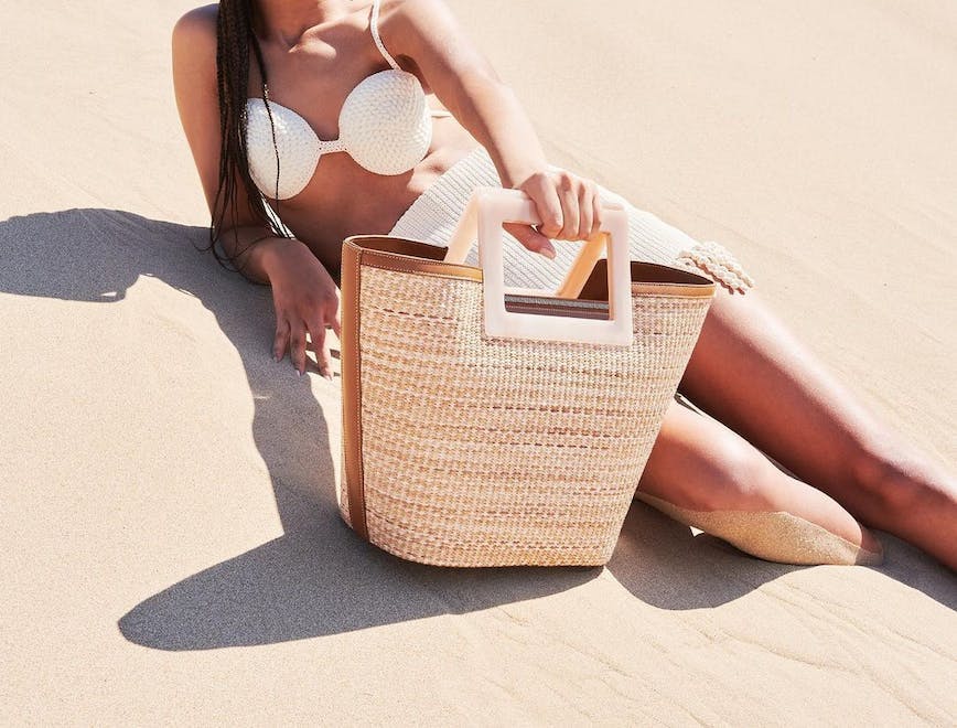 A model posing with a light brown woven straw beach bag