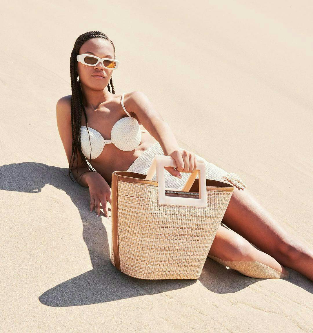 A model posing with a light brown woven straw beach bag