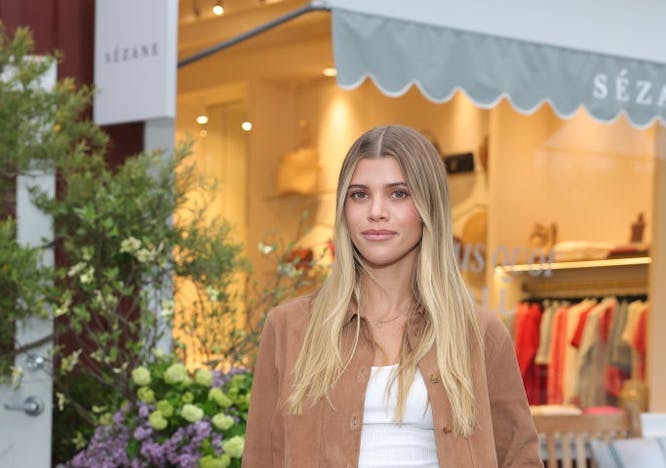 sofia richie in a camel colored jacket, white top, and black pants
