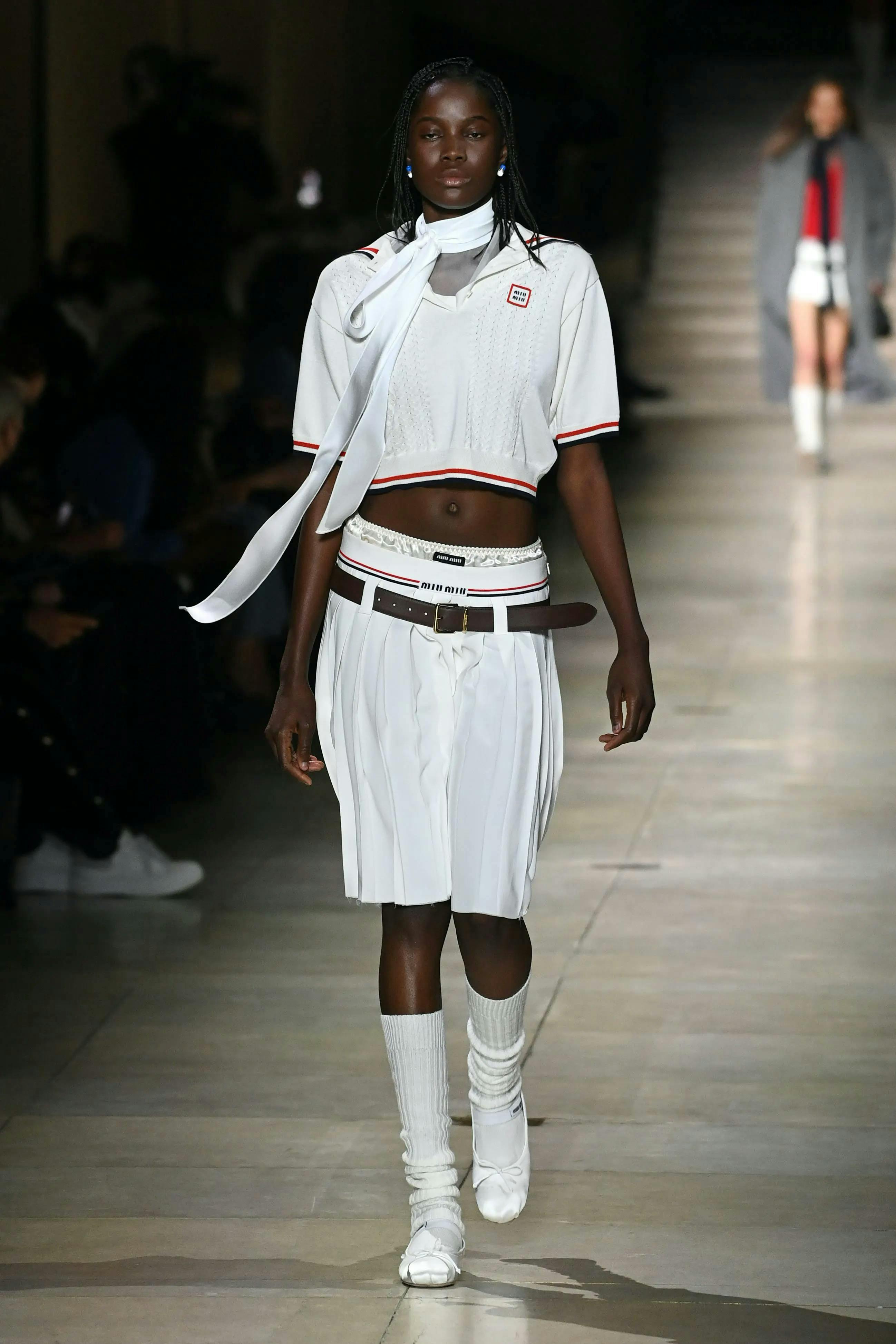 model in white flats, white polo shirt, and white knee length skirt