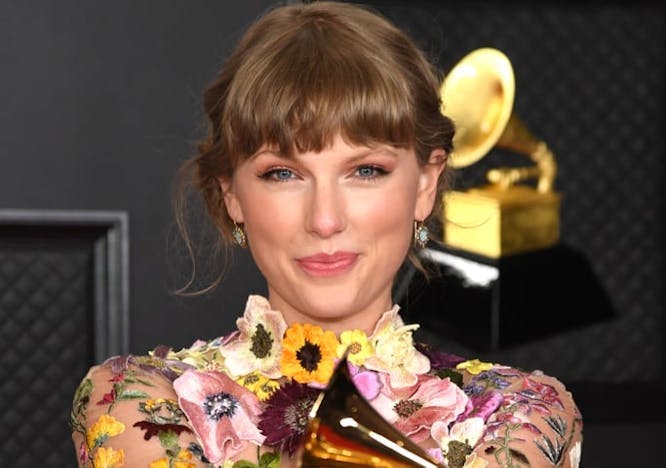Taylor Swift at the 2021 Grammys wearing a floral dress and holding out her Album of the Year Grammy