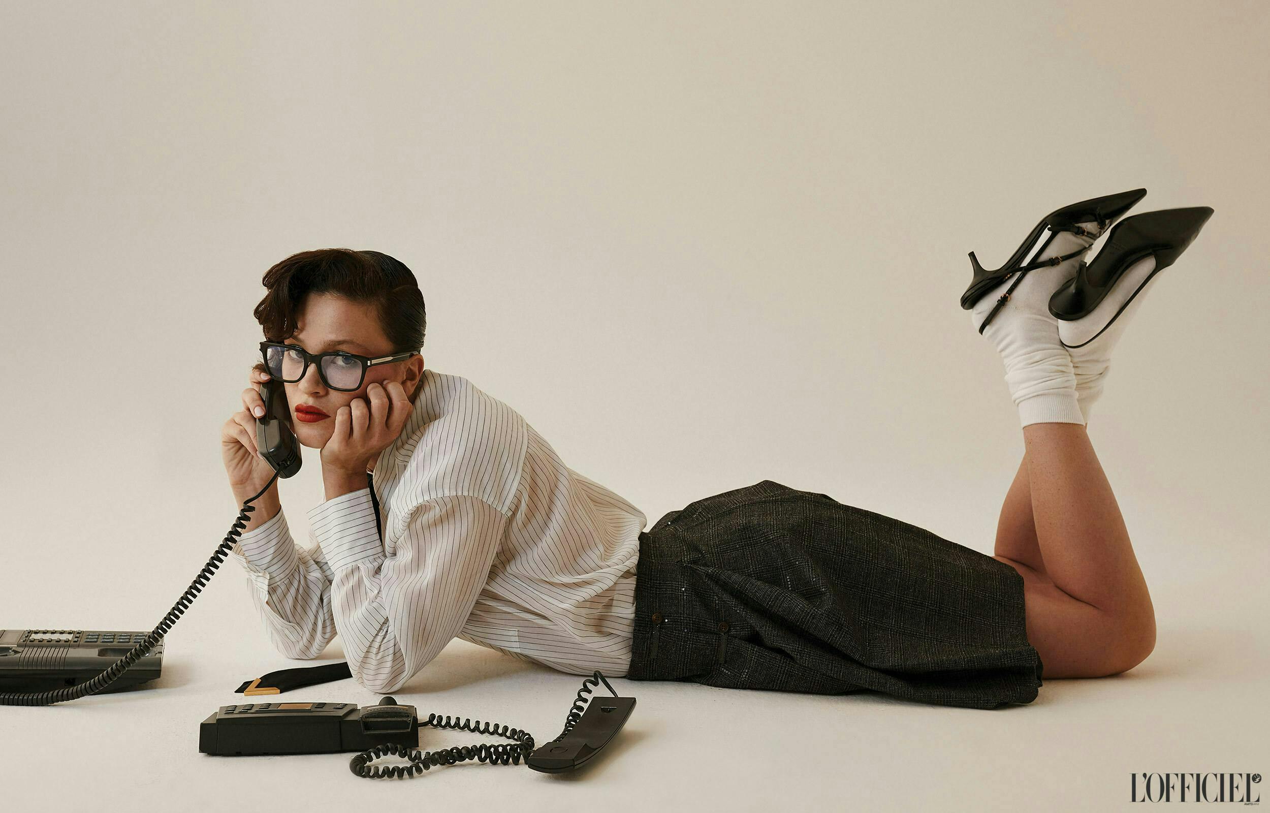 Model holding a landline phone in a shirst, skirt, heels, and glasses