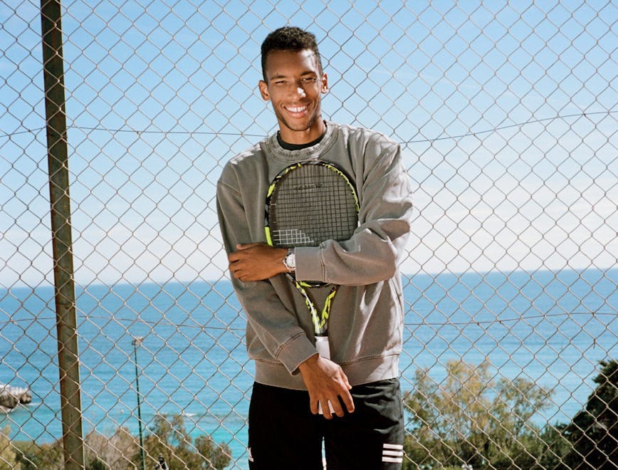 Félix Auger-Aliassime in a grey sweatshirt and black shorts holding a tennis racker