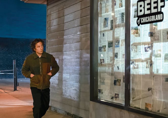 Jeremy Allen White as Carmy walking outside of sandwich shop with a sign that reads "The Original Beef of Chicagoland