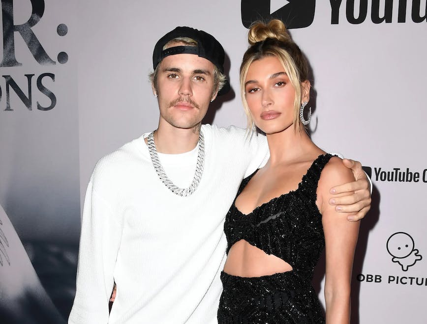 justin bieber, wearing white shirt and pink pants, with hailey bieber, wearing black dress