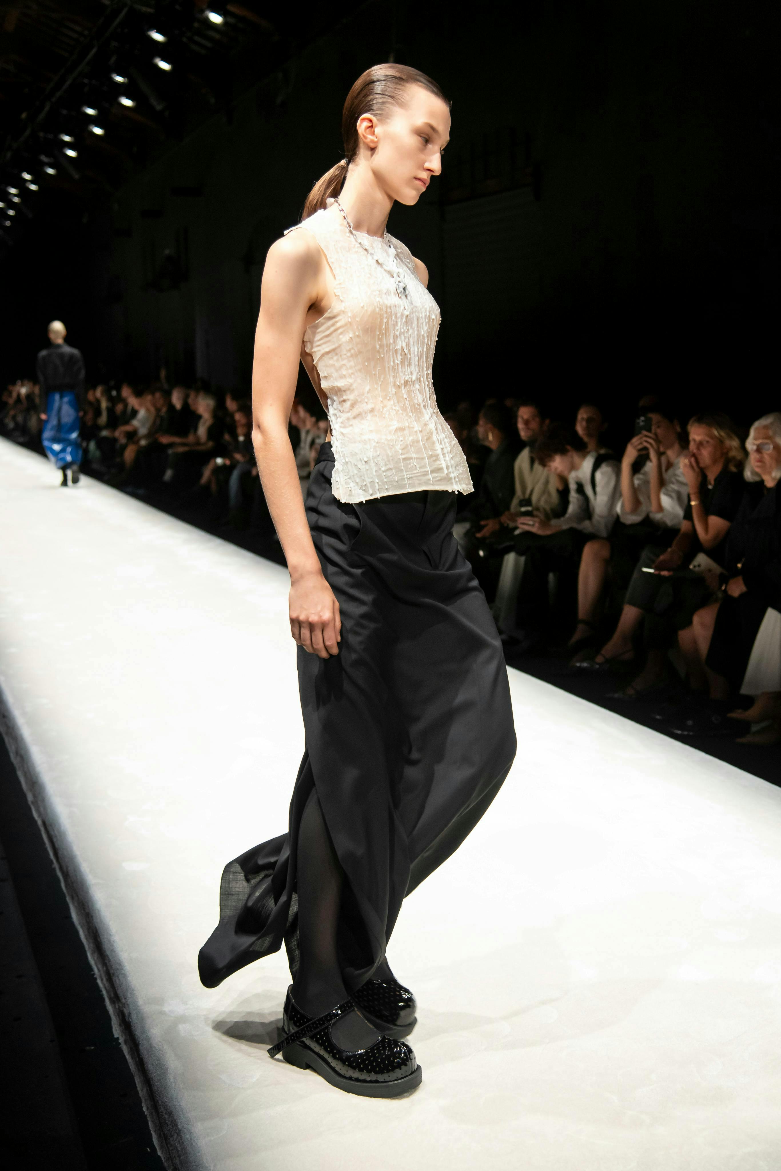 model on runway wearing white top and black pants