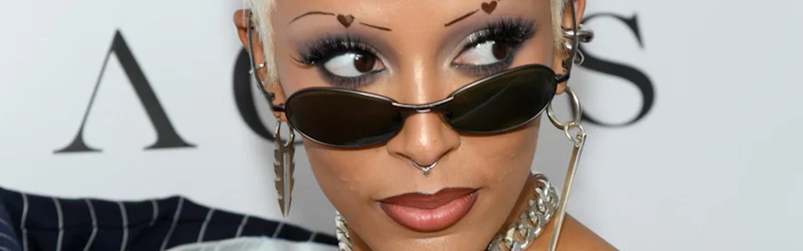 doja cat with pinstripe top, black sunglasses, and heart eyebrows