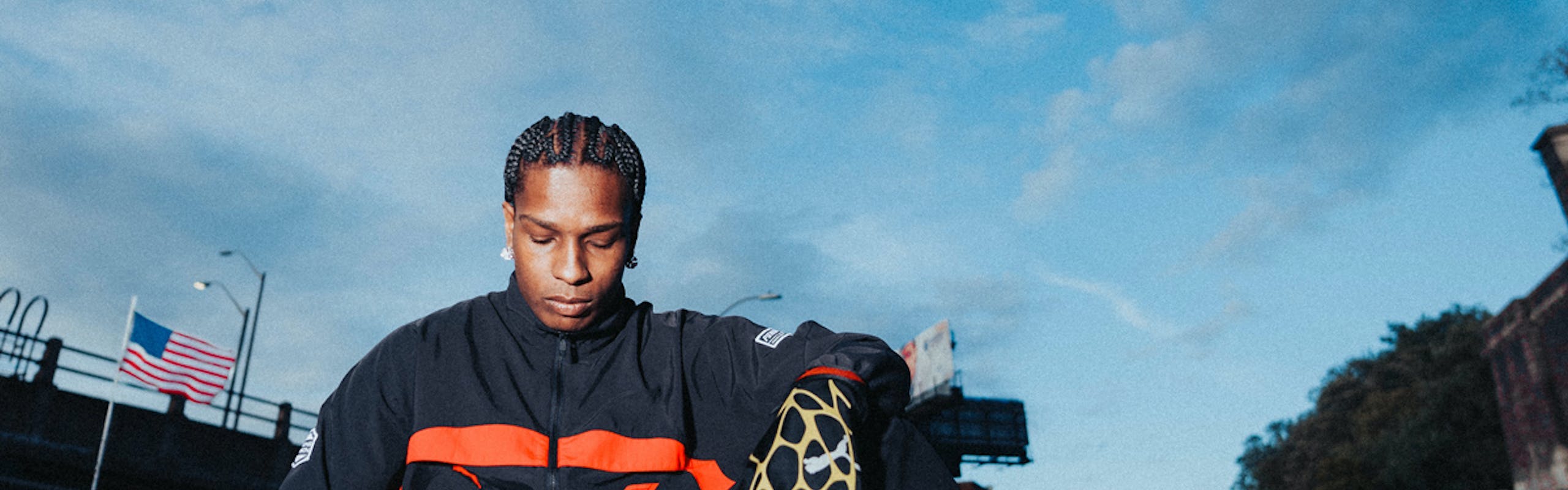 asap rocky in a black and orange racing suit sitting atop a car