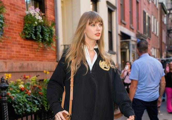 taylor swift in black rugby shirt with no pants holding a small brown crossbody