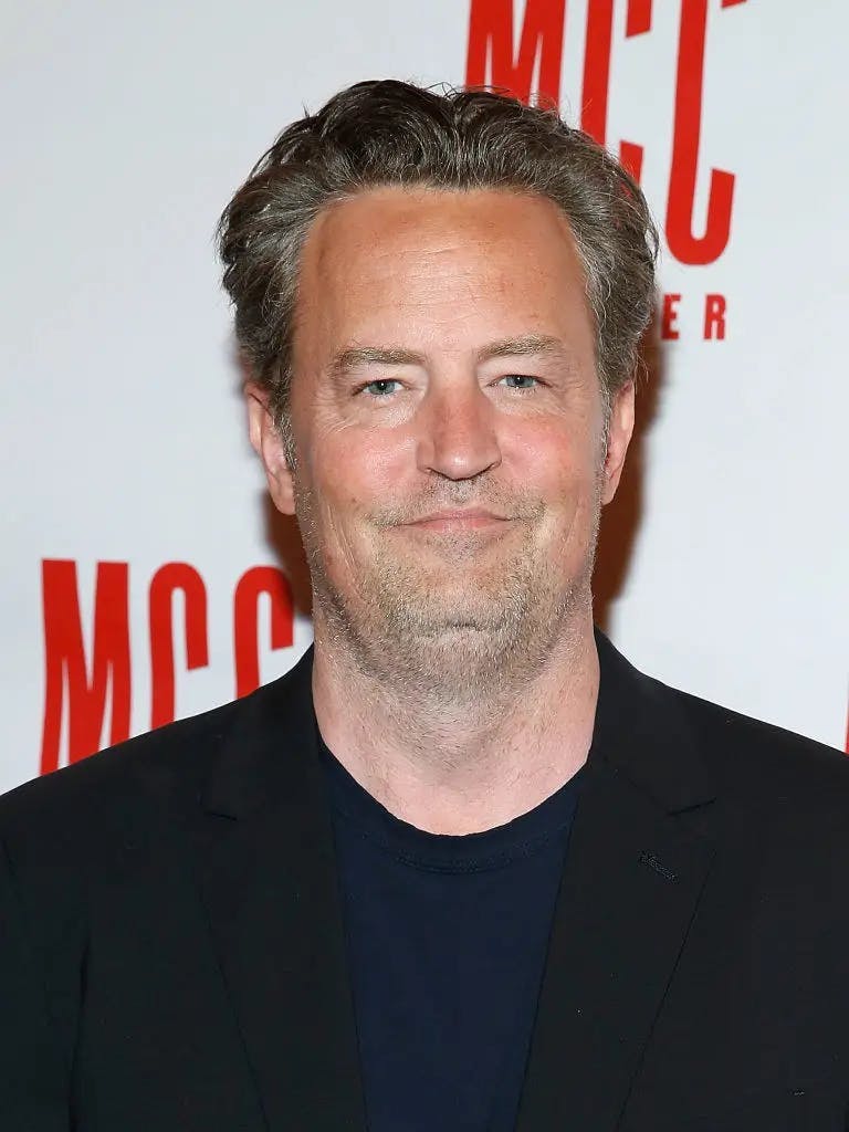matthew perry in black top looking at the camera