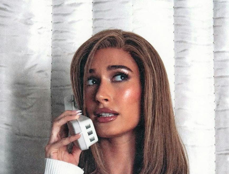 hailey bieber dressed as carmen electra with brown lob and white cardigan talking on the phone
