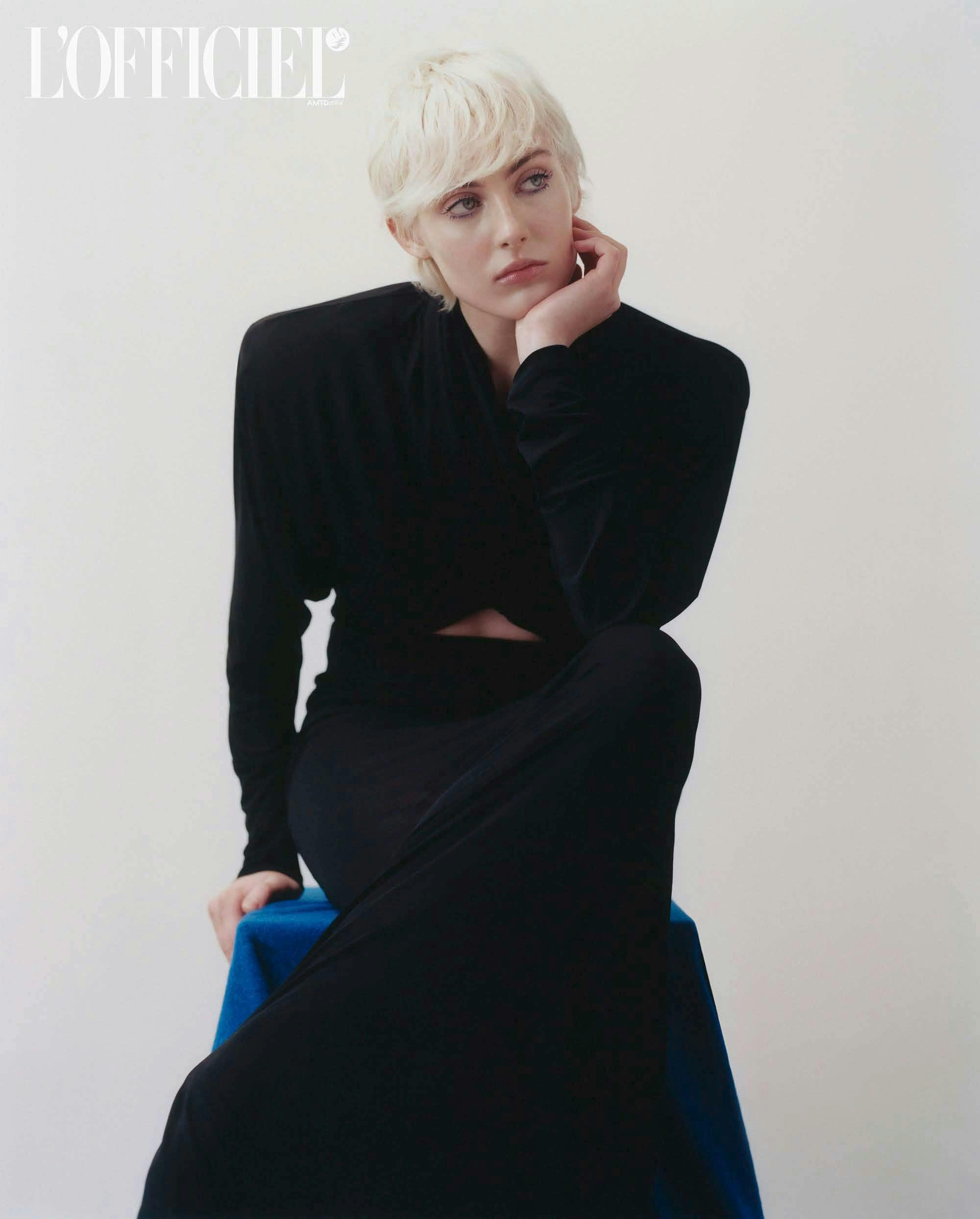 a model in a black dress sitting on a stool